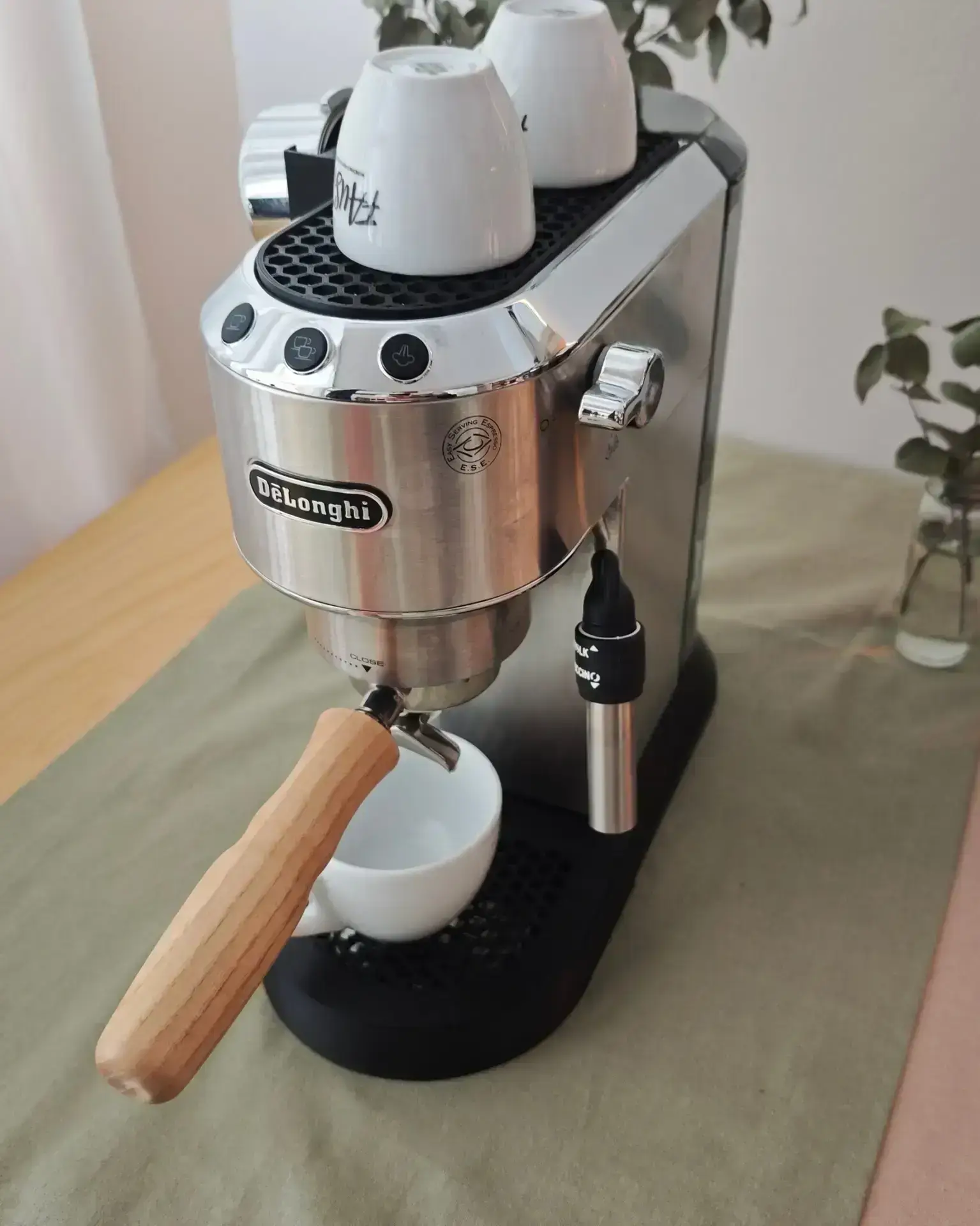 De'Longhi Dedica completa di vaschetta raccogligocce, poggiatazze e supporto portafiltro, tazze bianche e fiori sul tavolo della cucina