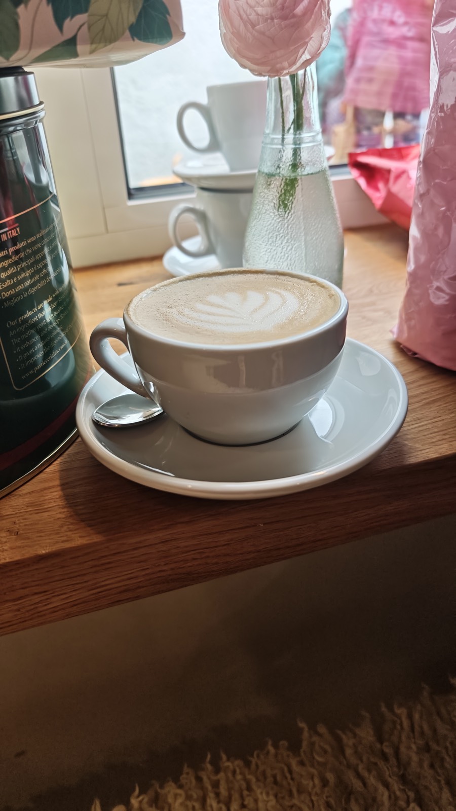 Cappuccino con latte art su un davanzale in legno, accanto un fiore in un vaso di vetro